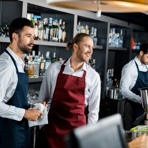 handsome cheerful barmen in aprons standing at workplace