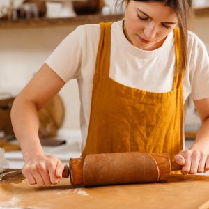 Caucasian focused pastry chef woman making dough with rolling pin at cozy kitchen