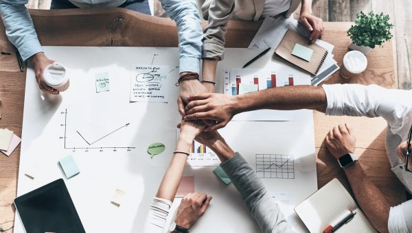 Successful team. Close up top view of business colleagues holding hands on top of one another in a symbol of unity while sitting in the creative office