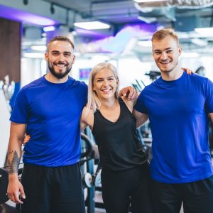 Three happy young people standing at the gym, hugging. Team and teamwork.
