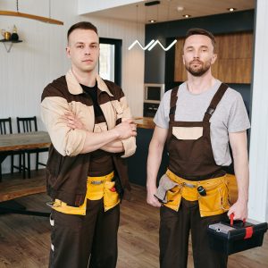 Two plumbers or repairmen in workwear standing in large domestic room